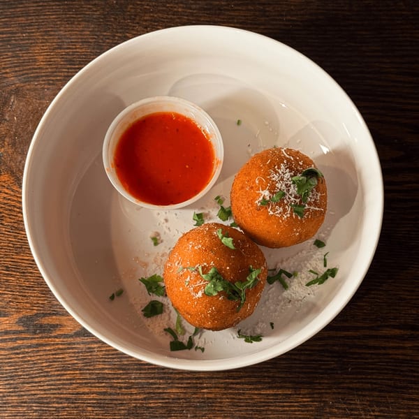 Two golden-brown arancini balls with parmesan and parsley, served with a side of marinara sauce.