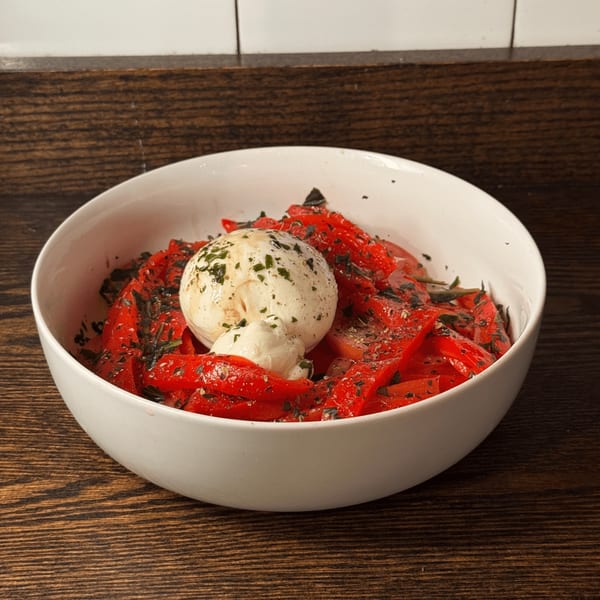 A white bowl filled with roasted red peppers, herbs, and a large dollop of burrata cheese.