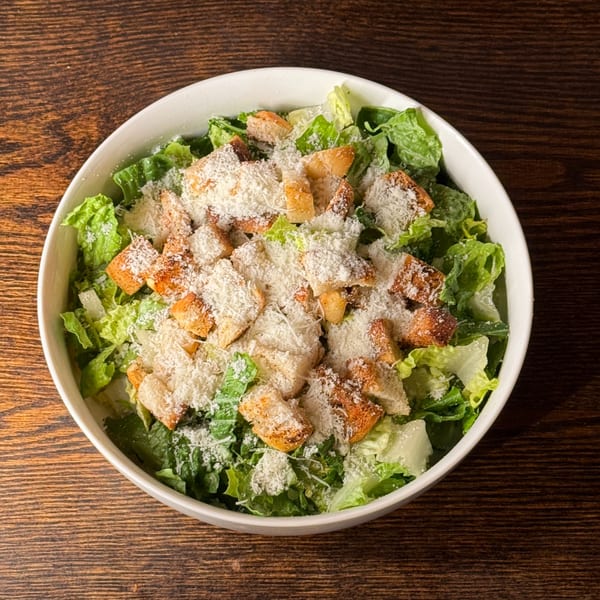 A white bowl of Caesar salad with romaine lettuce, croutons, and grated Parmesan cheese.