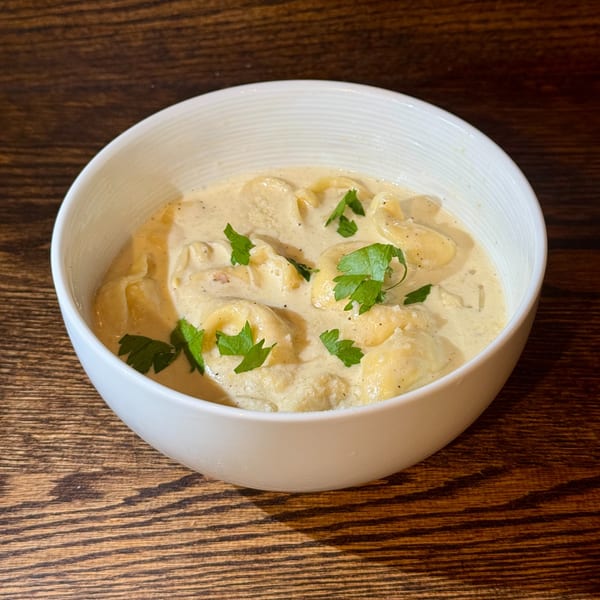 Creamy tortellini pasta with fresh parsley in a white bowl on a wooden table.