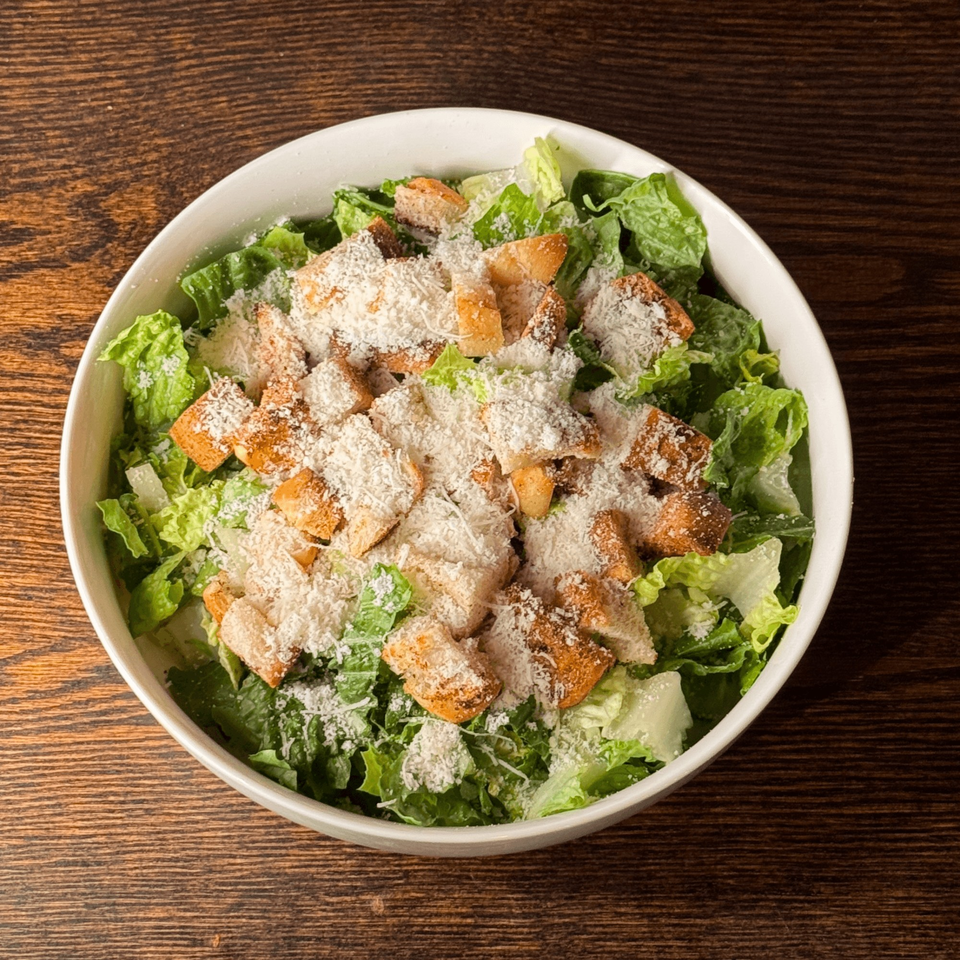 A white bowl of Caesar salad with crisp romaine, croutons, and grated Parmesan cheese.