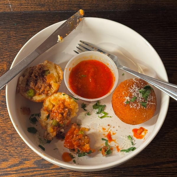 A plate of Rosa's Pizza arancini, some broken open, with a side of marinara sauce.