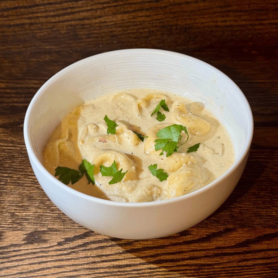 Creamy tortellini pasta dish with fresh parsley in a white bowl on a wooden table.