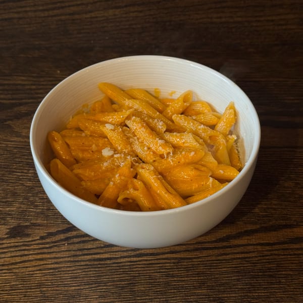 A white bowl filled with penne pasta in a creamy orange sauce, topped with grated cheese.