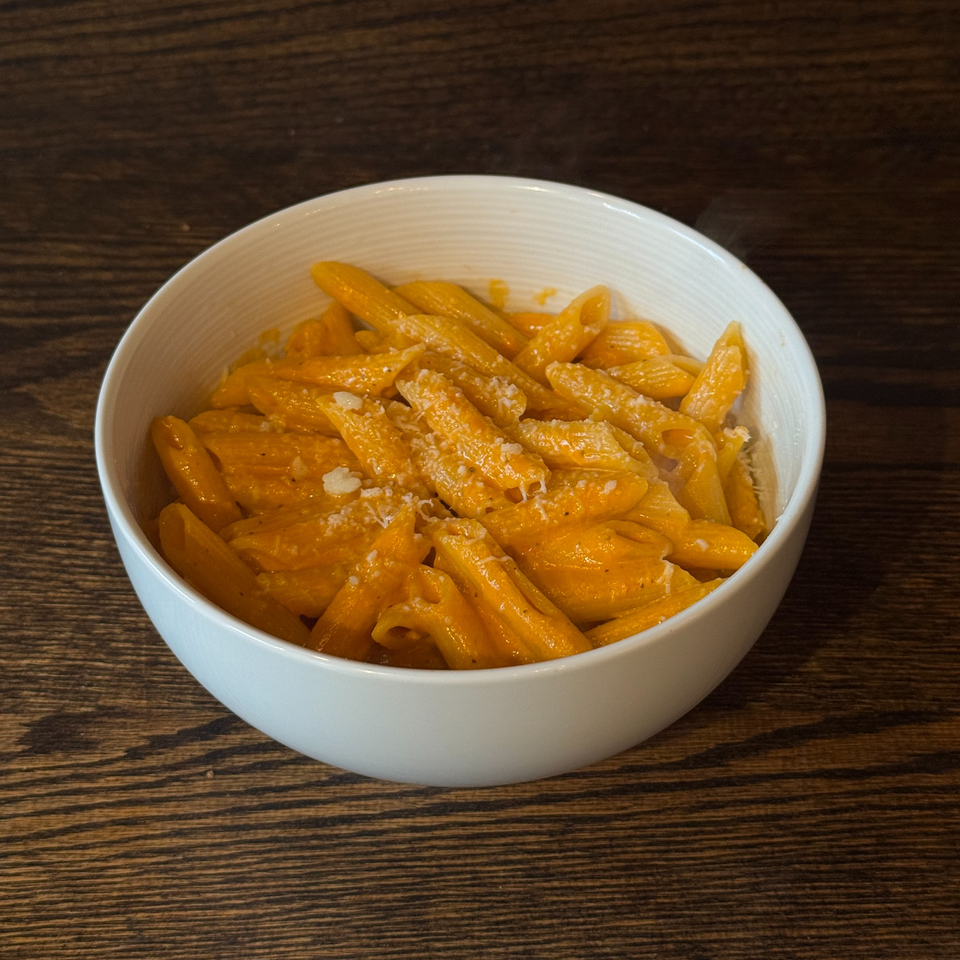 A white bowl filled with penne pasta in a creamy orange sauce, topped with grated cheese.