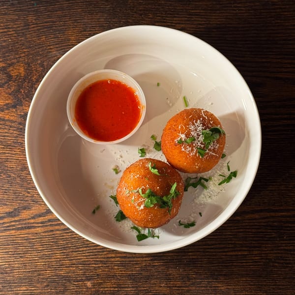 Two golden-brown arancini balls with grated cheese and parsley, served with a side of marinara sauce.