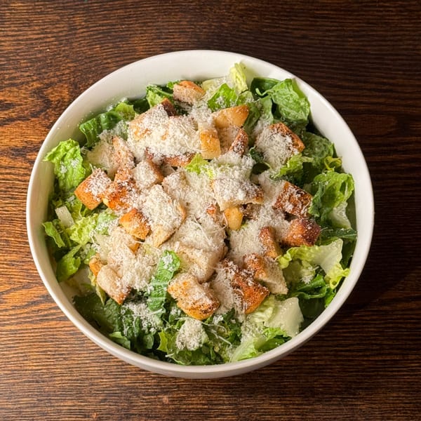 A white bowl filled with fresh Caesar salad, topped with croutons and grated Parmesan cheese.