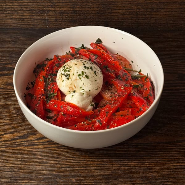 A white bowl filled with roasted red peppers, topped with a ball of burrata cheese and herbs.