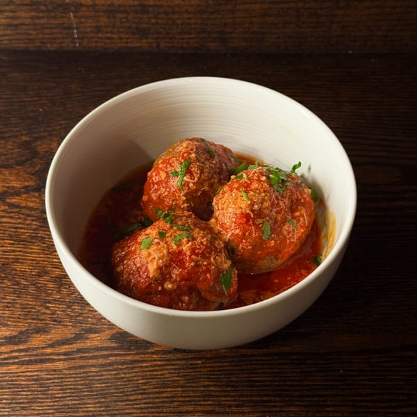 Three large meatballs in marinara sauce, topped with grated cheese and parsley, in a white bowl.