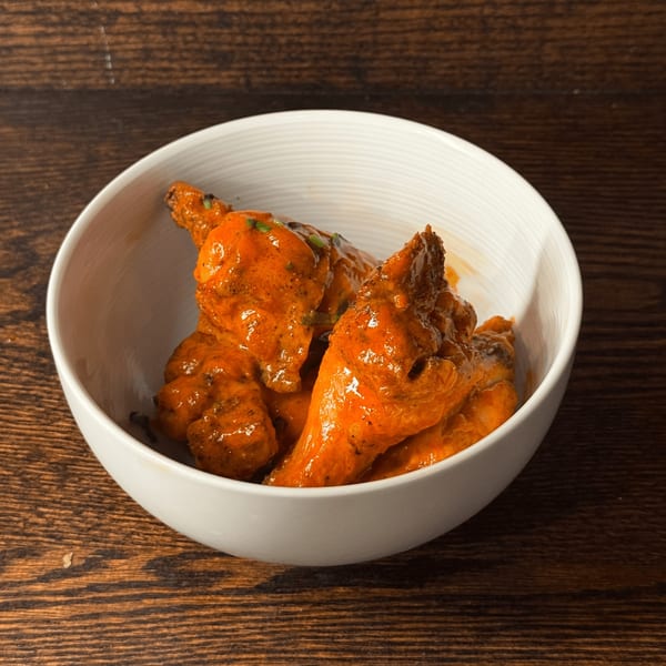 A white bowl filled with Rosa's Pizza's buffalo chicken wings, garnished with green herbs.