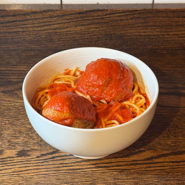 A white bowl filled with spaghetti and two large meatballs covered in red marinara sauce.