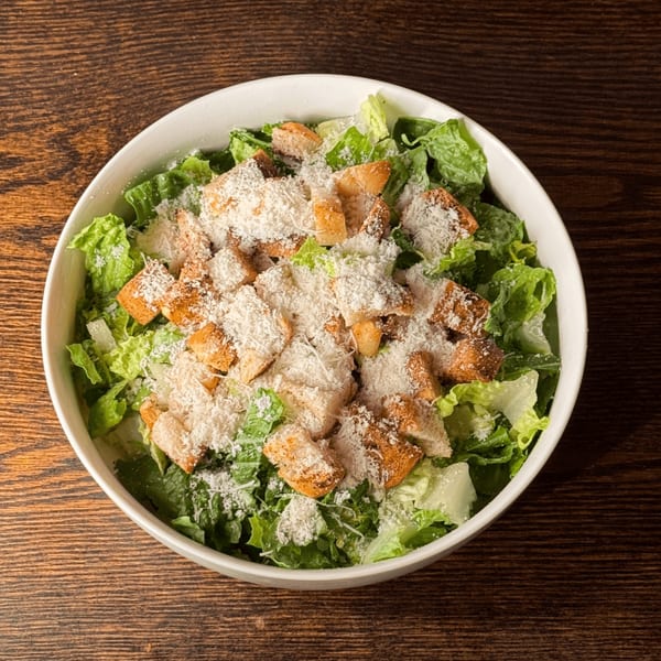 A white bowl of Caesar salad with crisp romaine, croutons, and grated Parmesan cheese.