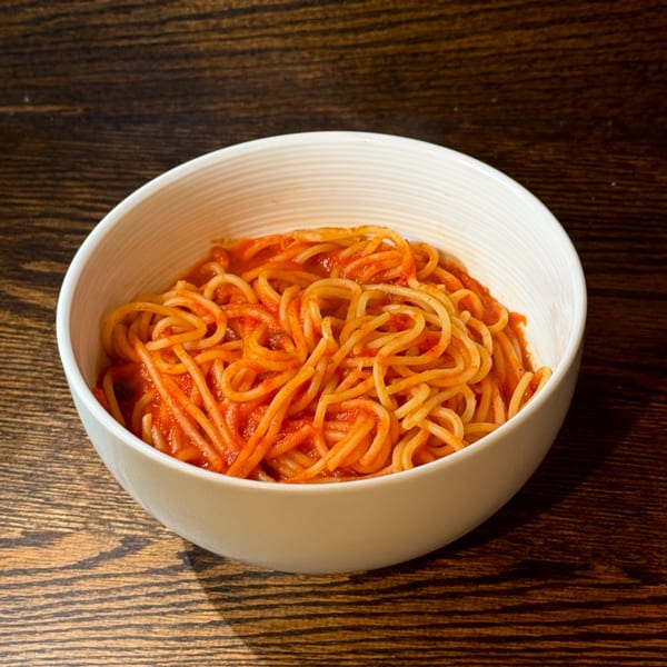 A white bowl filled with spaghetti and red tomato sauce, on a dark wooden table.