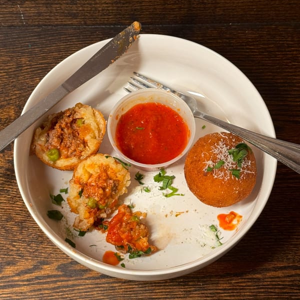 Partially eaten arancini with meat and peas, served with marinara sauce on a white plate.