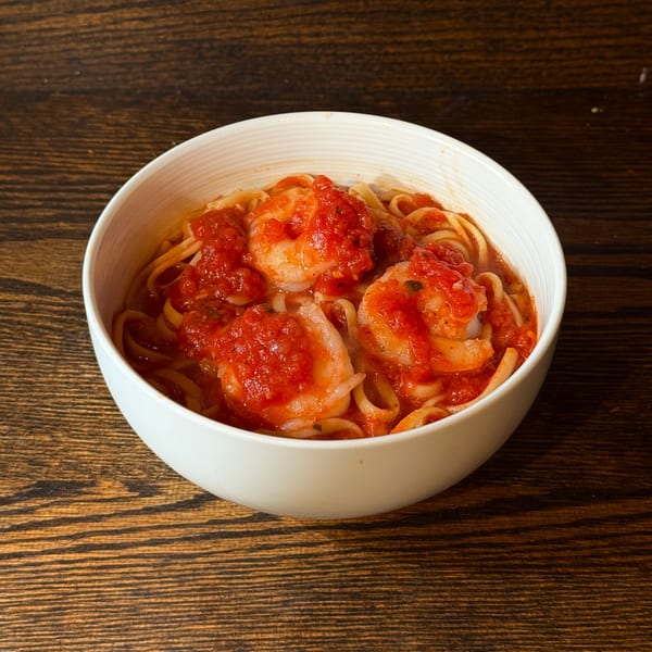 Shrimp linguine with red tomato sauce in a white bowl on a wooden table.
