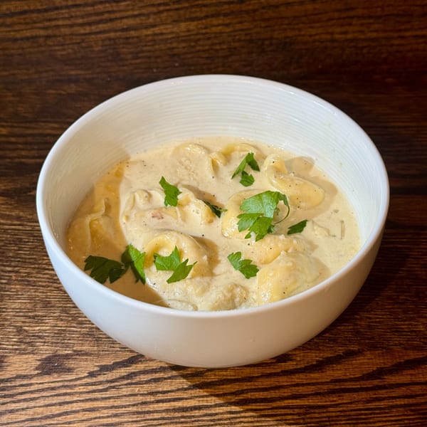 Creamy tortellini pasta dish with fresh parsley in a white bowl on a wooden table.