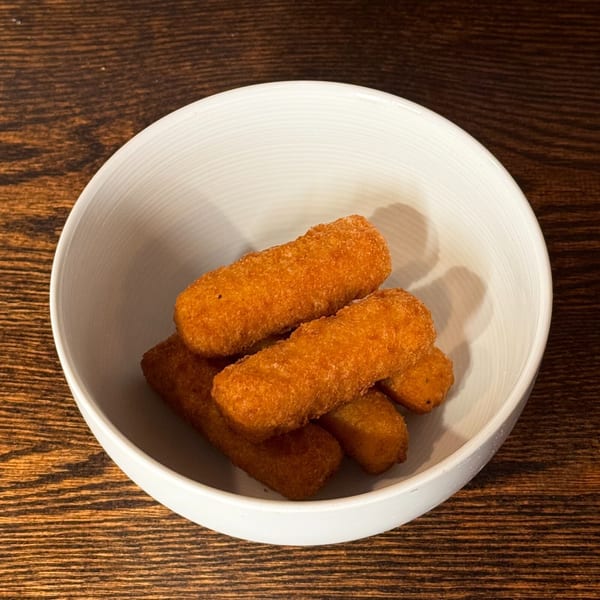 A white bowl filled with several golden-brown, breaded mozzarella sticks on a wooden table.