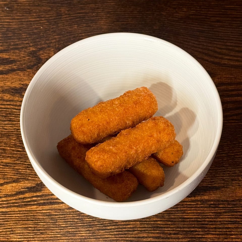 A white bowl filled with several golden-brown, breaded mozzarella sticks on a wooden table.