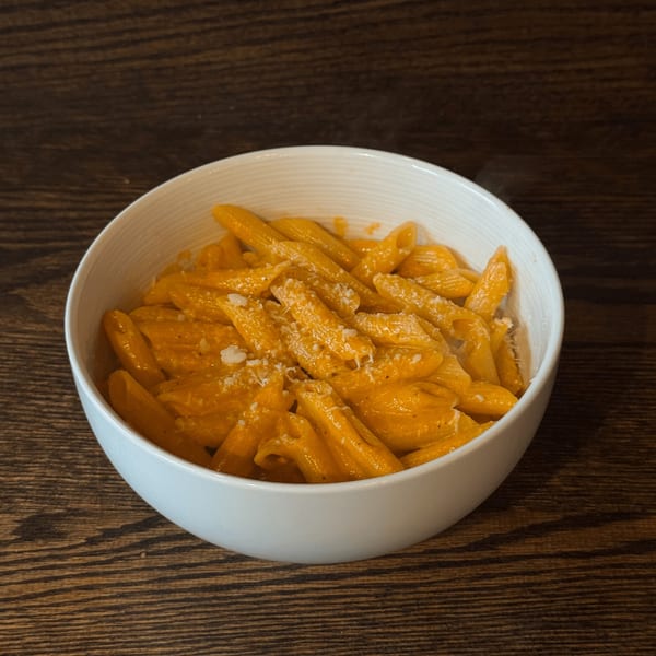 A white bowl filled with penne pasta in a creamy orange sauce, topped with grated cheese.