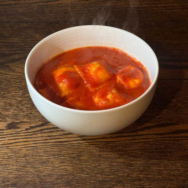 Steaming ravioli in a rich red tomato sauce, served in a white bowl on a wooden table.