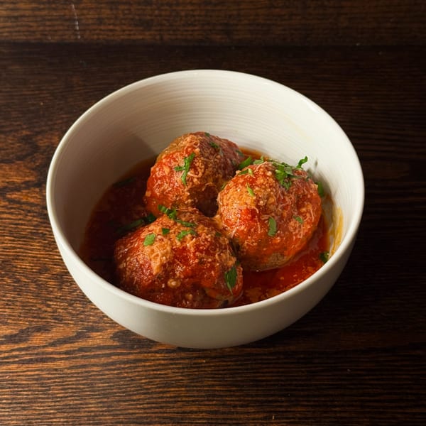 Three large meatballs covered in red sauce, parmesan cheese, and parsley in a white bowl.