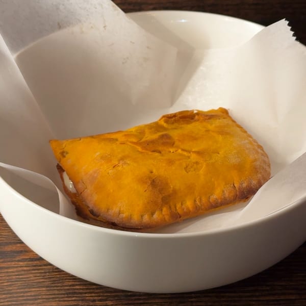 A golden-brown Rosa's Pizza pepperoni roll, served in a white bowl lined with parchment paper.