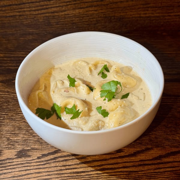 Creamy tortellini pasta dish, garnished with fresh parsley, in a white bowl on a wooden table.
